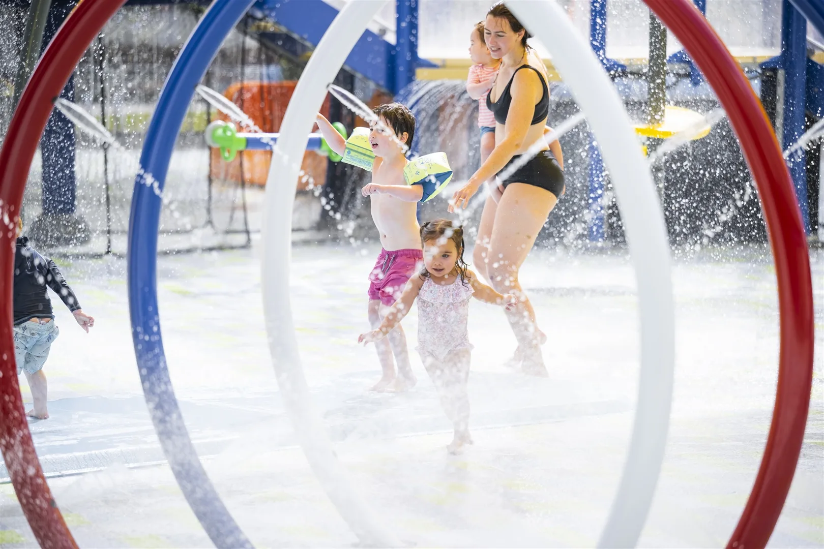 Children and mother playing in colorful water playground with spray arches and splash features at aquatic center